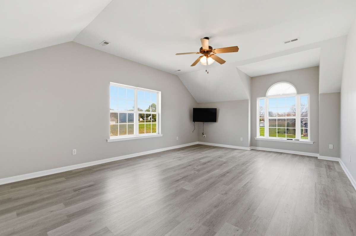 Large versatile bonus room with vaulted ceilings and durable flooring, perfect for a media room, home office, or playroom.