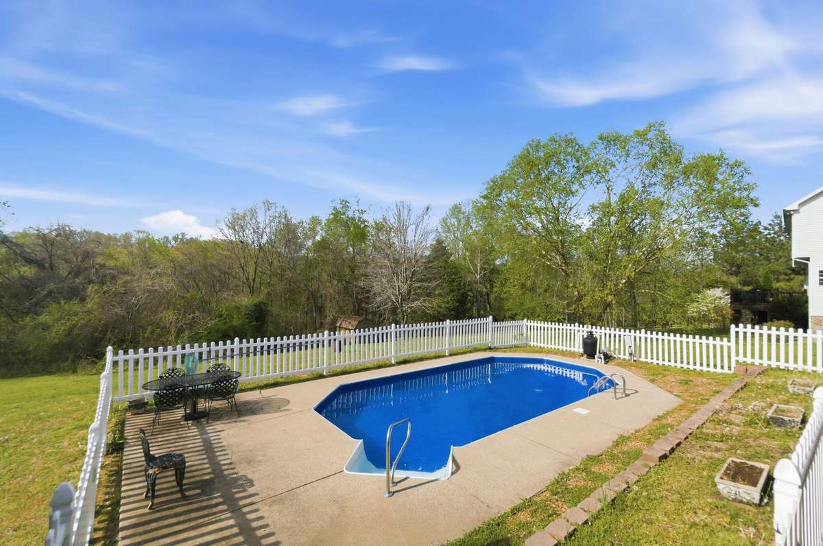 Private in-ground pool surrounded by a spacious concrete deck and fully enclosed with a white picket fence, creating a perfect setting for outdoor enjoyment.
