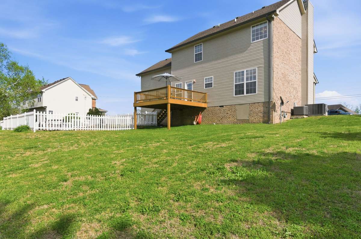 Rear view of the home showcasing the elevated deck, fenced pool area, and generous backyard space.