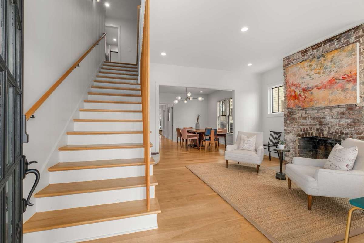 The front entry living space greets visitors with periodic specific components dating back to the historic original bungalow home.  Note the large case opening, overhead lighting, brick fireplace (decorative only), and light colored hardwood floors.