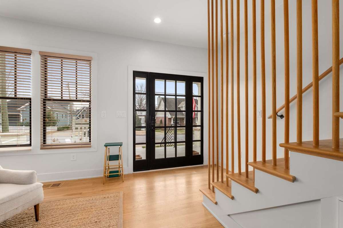 Alternate view of front main entry and large windows, glass front door, and decorative trim railing detail leading to the second floor.