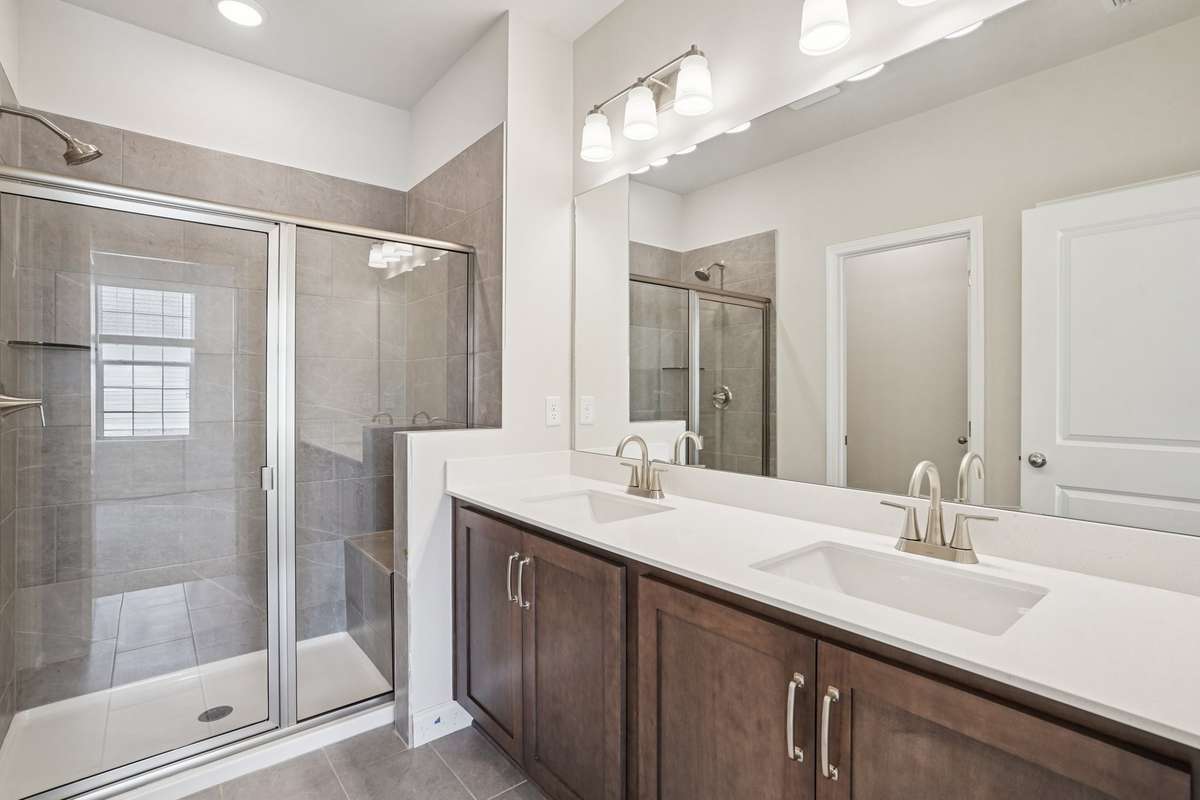 The Primary Bath showcases tile flooring, dual vanities with quartz countertops, and a beautifully tiled shower complete with a convenient built-in bench seat for added comfort and style.