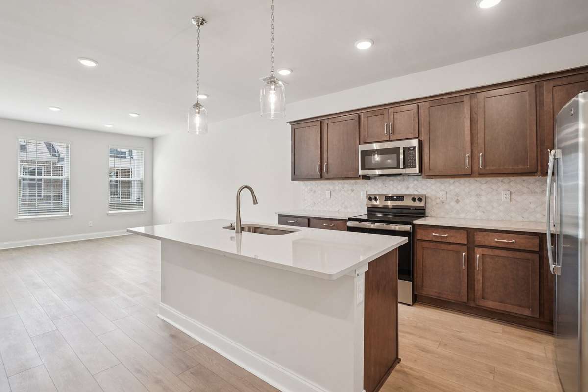 The kitchen features wood-toned cabinetry with soft-close doors, quartz countertops, and a mosaic backsplash, creating a bright, modern, and highly functional space.