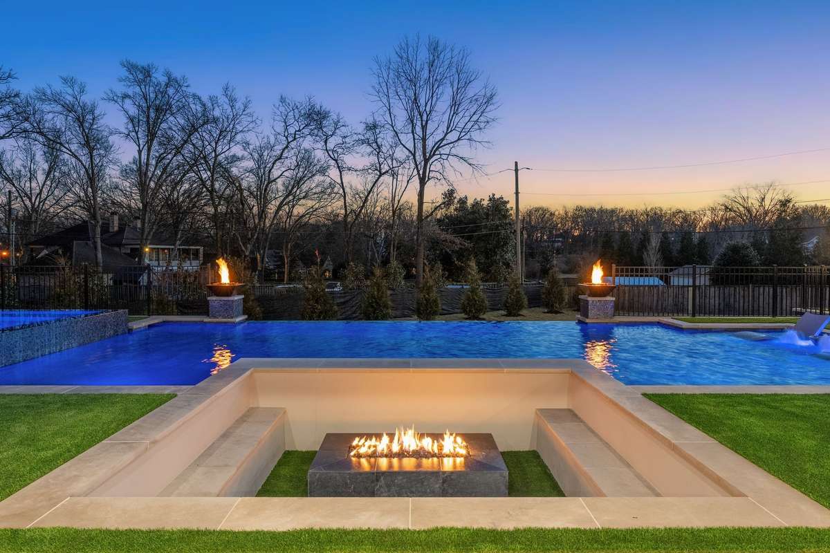 Custom pool with sun shelf, integrated flame accents, and a sunken fire pit lounge overlooking the private grounds.