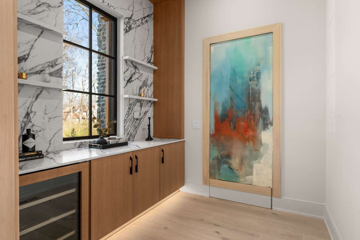 Adjacent to the home office, the bar area showcases dramatic marble, custom cabinetry, and a built-in wine refrigerator.