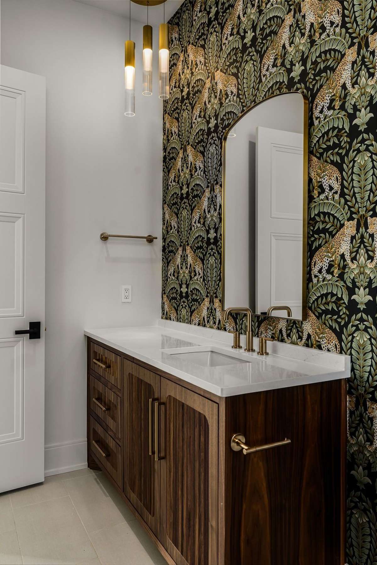 Designer bath with statement wallpaper, custom vanity, and elegant brass fixtures.