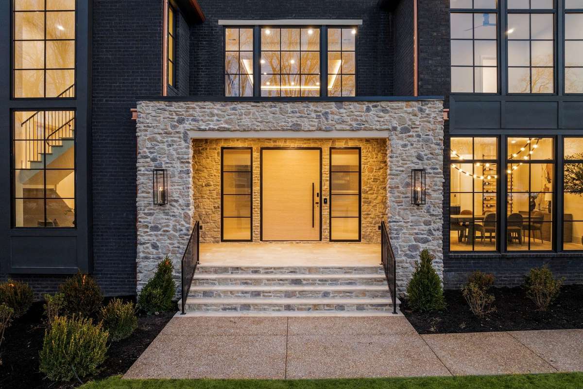 A commanding stone entry with gas lanterns introduces the home with scale, texture, and timeless character.