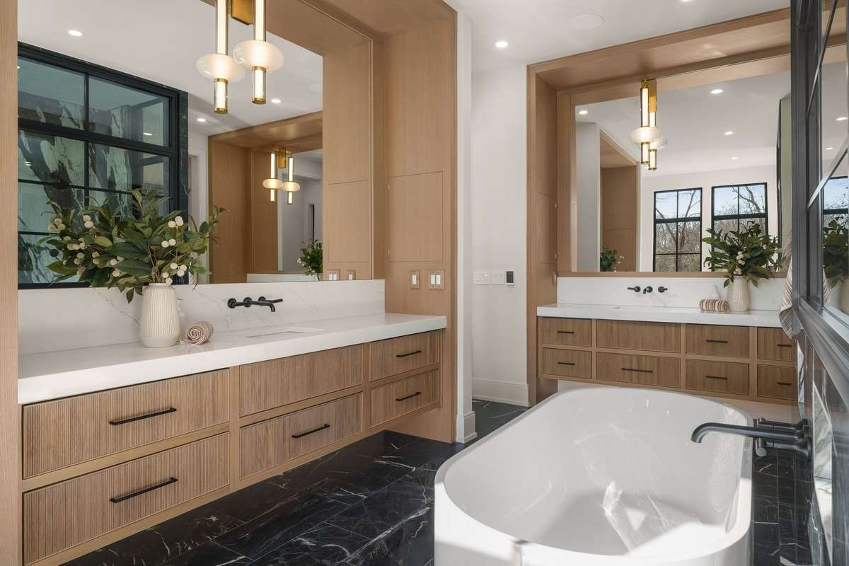 Sculptural in design yet highly functional, the spa-like primary bath features warm custom cabinetry, concealed medicine cabinets, and lighting reminiscent of fine art.