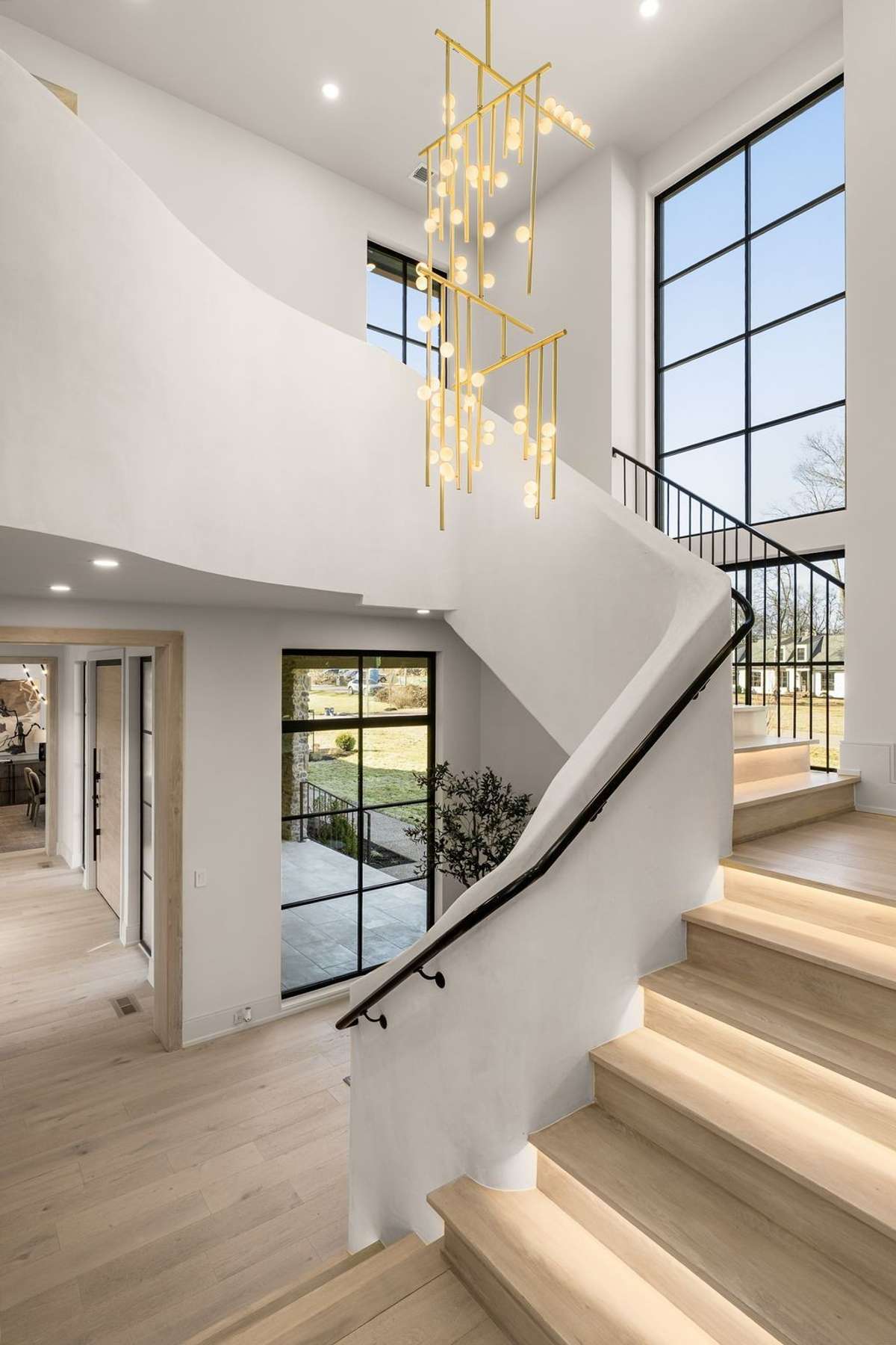 A sculptural chandelier and oversized windows turn the staircase into a stunning architectural centerpiece, filled with natural light and striking design.
