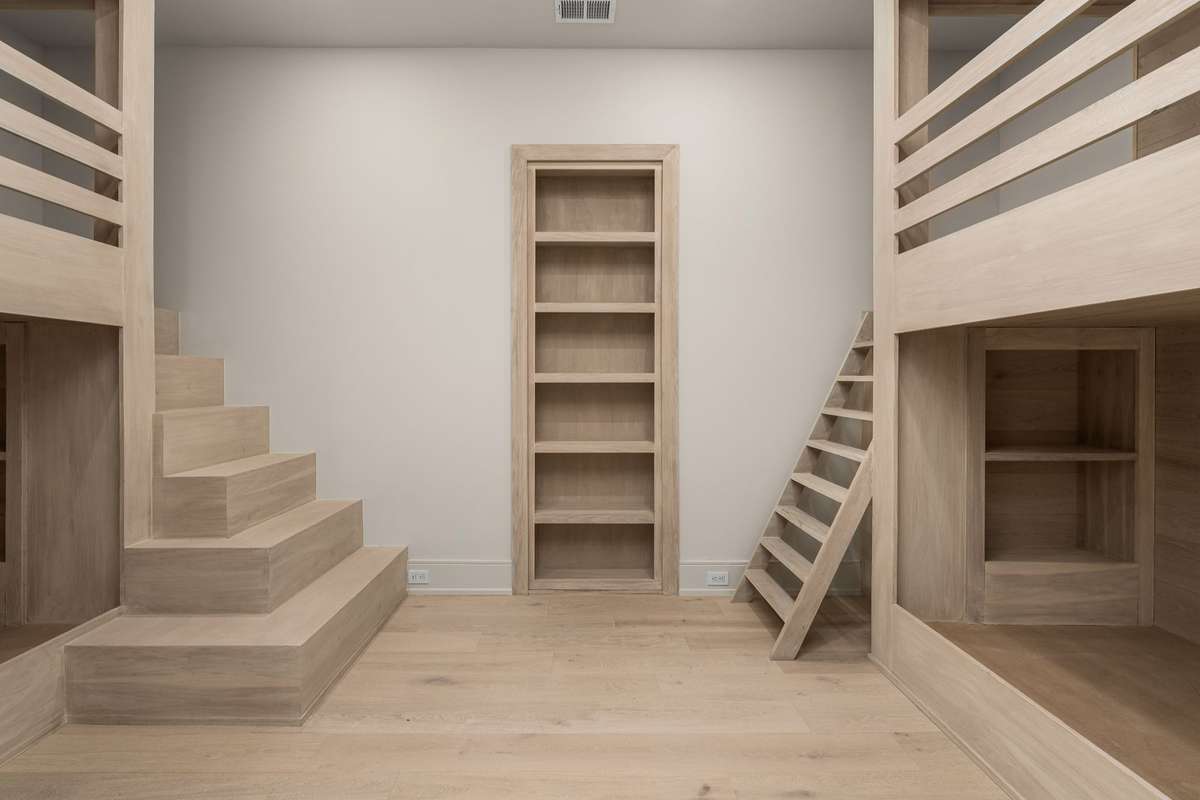 Custom bunk room with built-in shelving and ladders—perfect for sleepovers or extra holiday visitors. The bookcase doubles as a concealed door to the theater room.