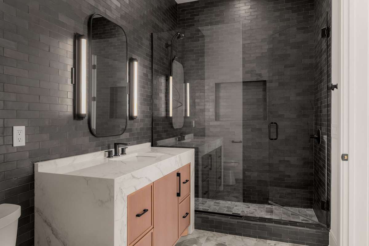 All upstairs bedrooms offer en-suite baths, each thoughtfully designed with distinctive finishes. This bath features full tiled walls and a frameless glass shower.