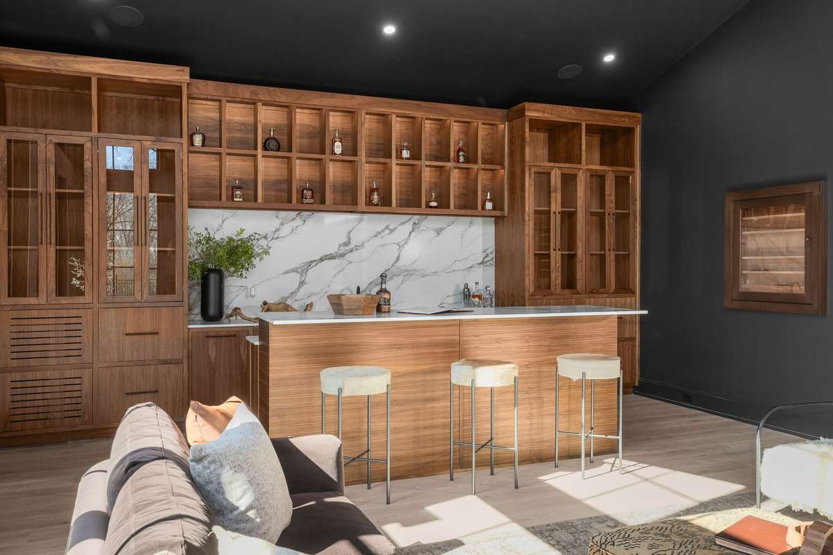 Wrapped in walnut, the bar features stone counters, lighted liquor display shelving, and island seating.