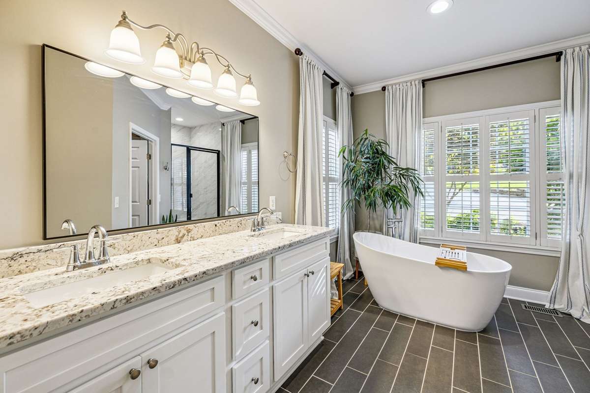 The large double vanity with granite, gray tone tile floors, standalone tub, and walk in shower make this primary bath just perfect