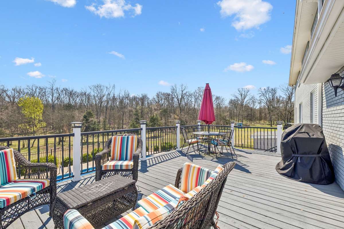 Elevated deck overlooks the wooded 17-acre property with wicker seating arranged for conversation and a grill ready for outdoor cooking.