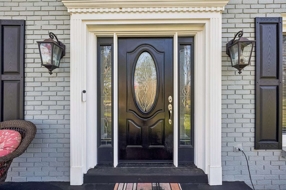 Elegant front entry with decorative glass sidelights and an oval window creates a welcoming first impression beneath the covered portico.