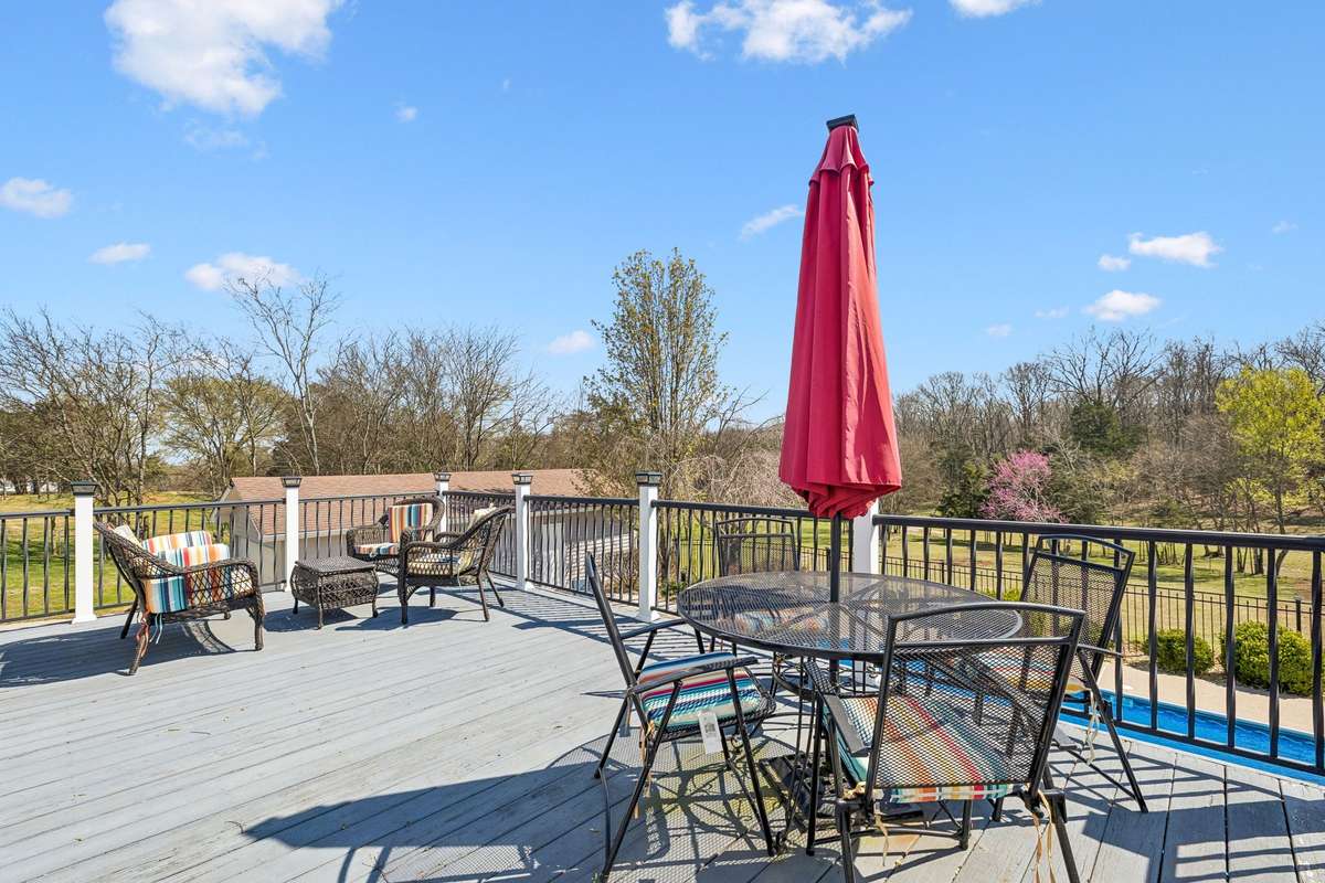 Elevated deck with outdoor dining setup overlooks the wooded 17-acre property and inground pool below.