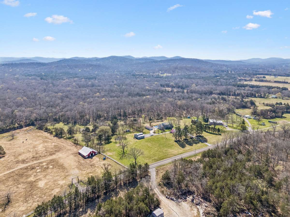 This elevated view reveals how the rolling Tennessee hills create a natural backdrop for the property, with the forested ridgeline extending for miles beyond the cleared pastures.