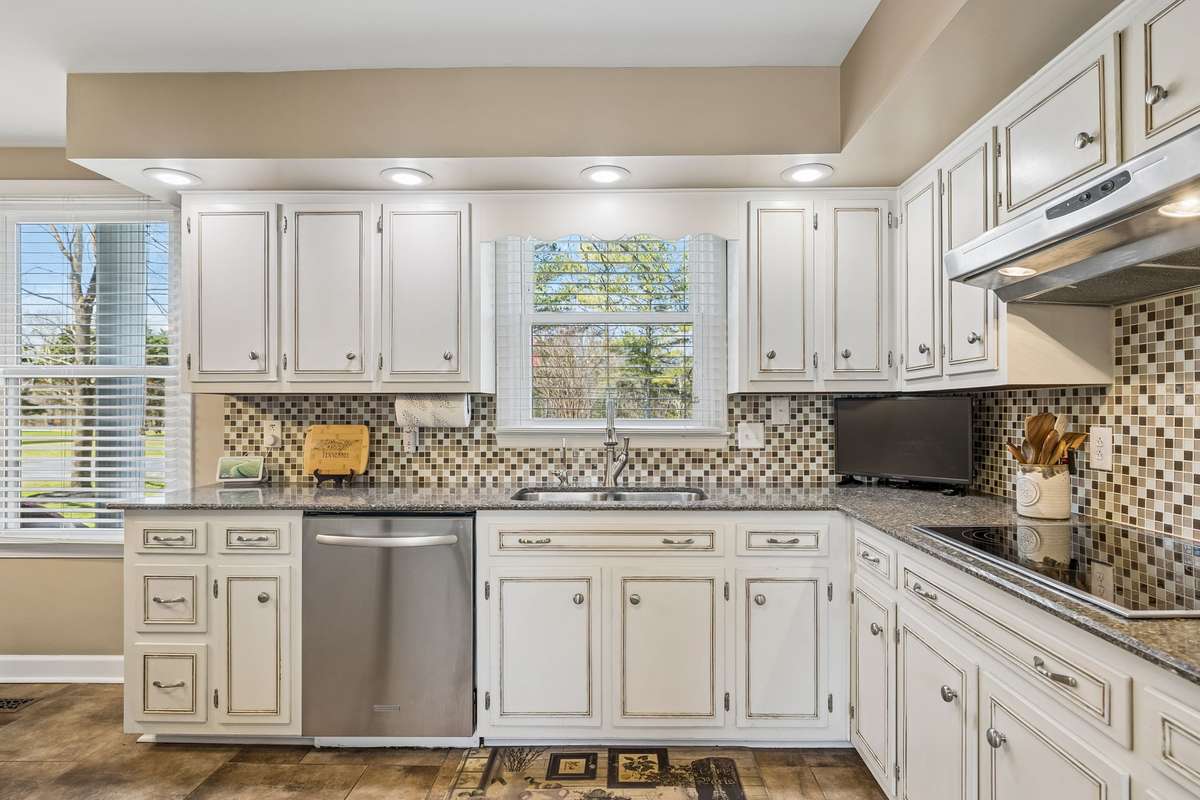 Updated kitchen with white cabinetry, granite counters, and mosaic tile backsplash creates a clean workspace with plenty of cabinet storage for organizing.