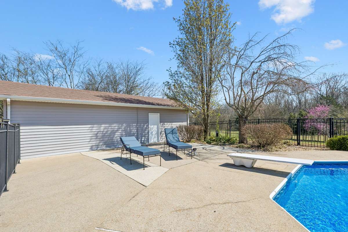 Pool deck extends along the garage side with diving board positioned for deep-end access and concrete decking that handles wet feet without getting slippery.