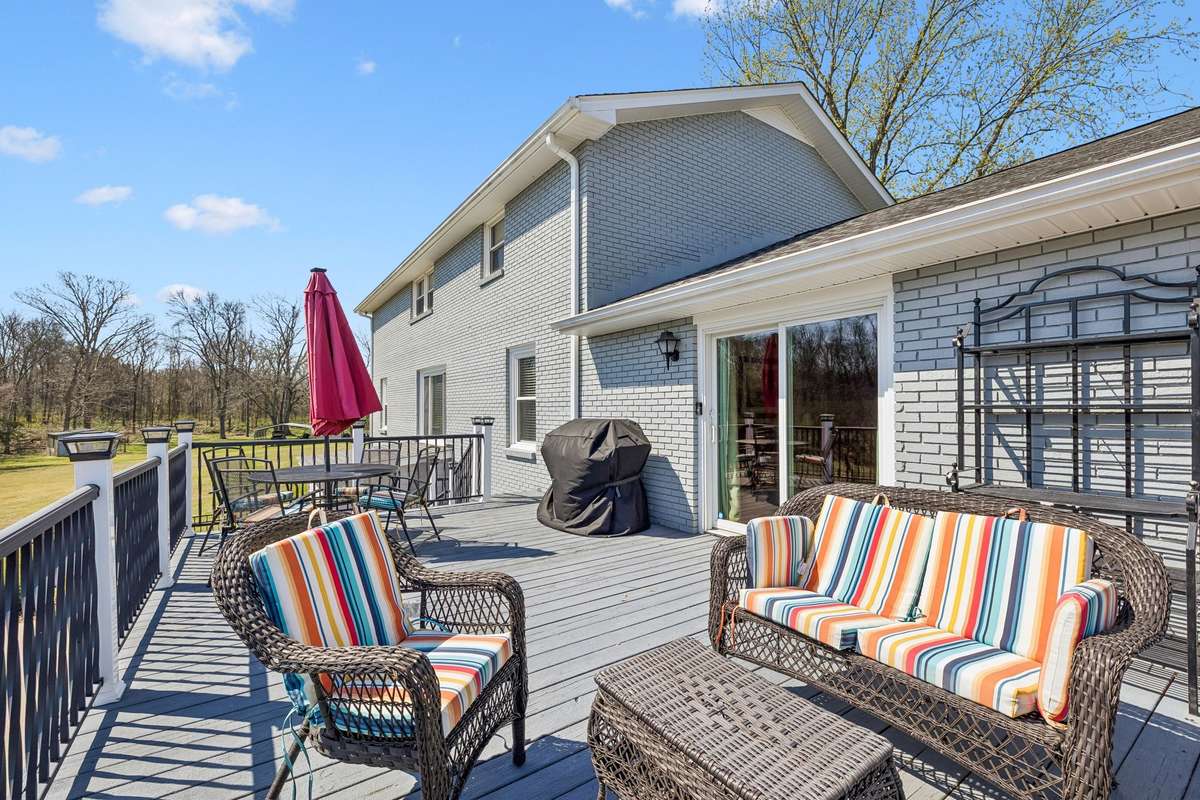 Elevated deck off the back of this Christiana home overlooks 17 wooded acres with wicker seating arranged for conversation and a grill ready for outdoor cooking.