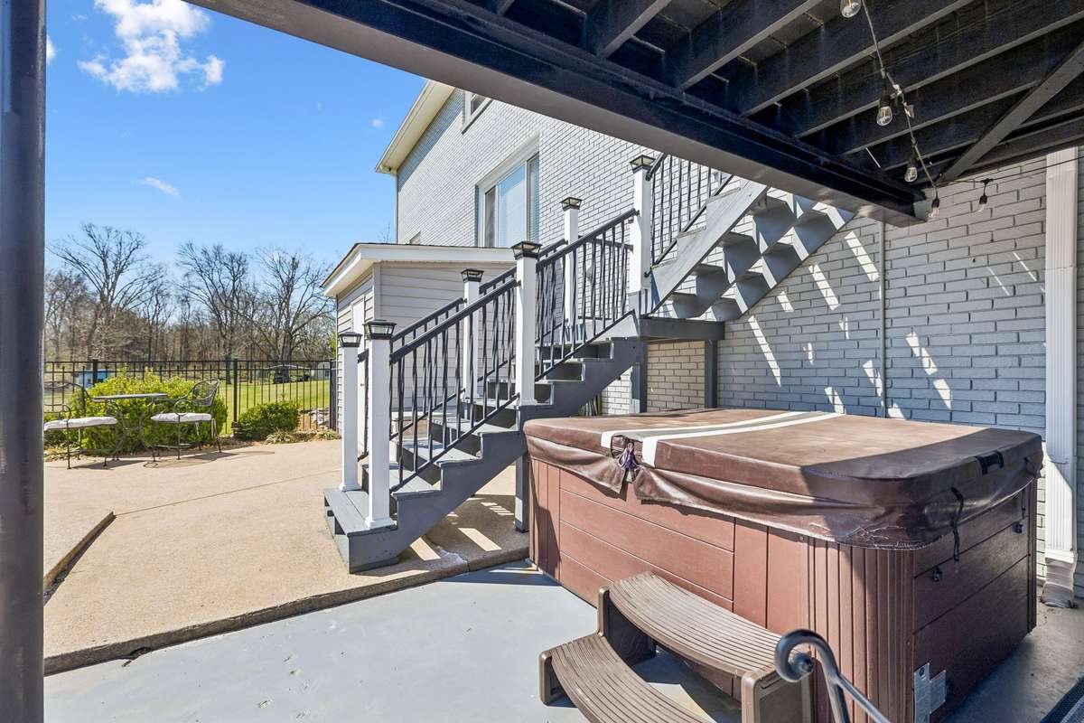 Hot tub positioned under the covered area stays protected from weather while still offering views across the wooded acreage.