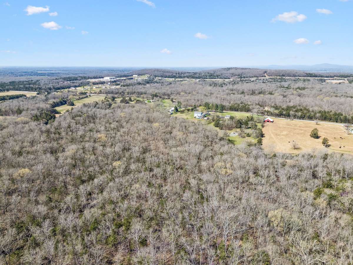 Aerial view showcases the property's 17 wooded acres with the red barn and cleared pasture areas creating a perfect balance of open space and natural forest buffer.