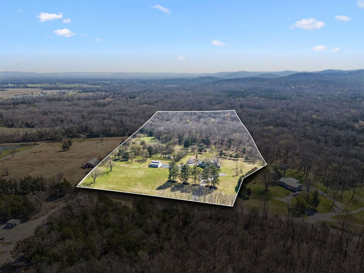 This aerial perspective showcases the full 17-acre property with its mix of open pasture, wooded areas, and the main home positioned among mature trees for natural privacy.
