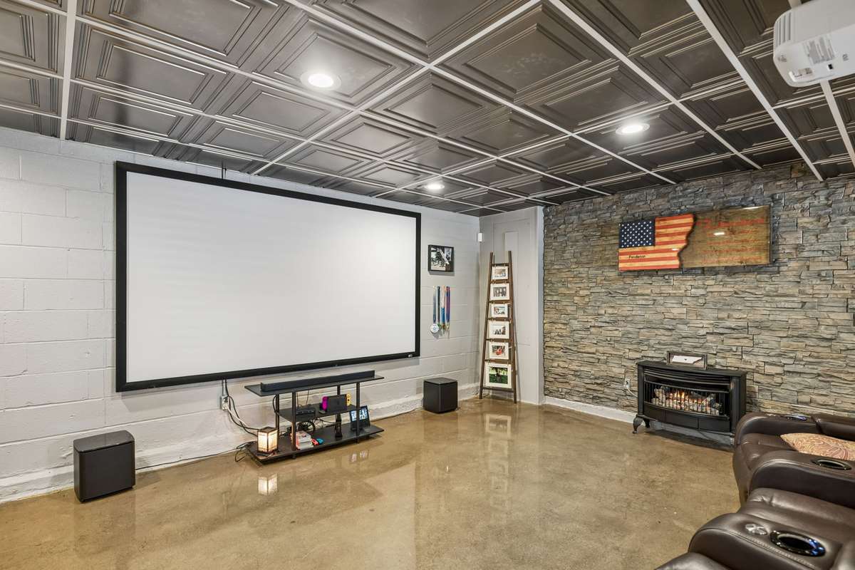 Recreation room with a stone fireplace wall and projector setup creates a comfortable spot to catch a game or watch movies.