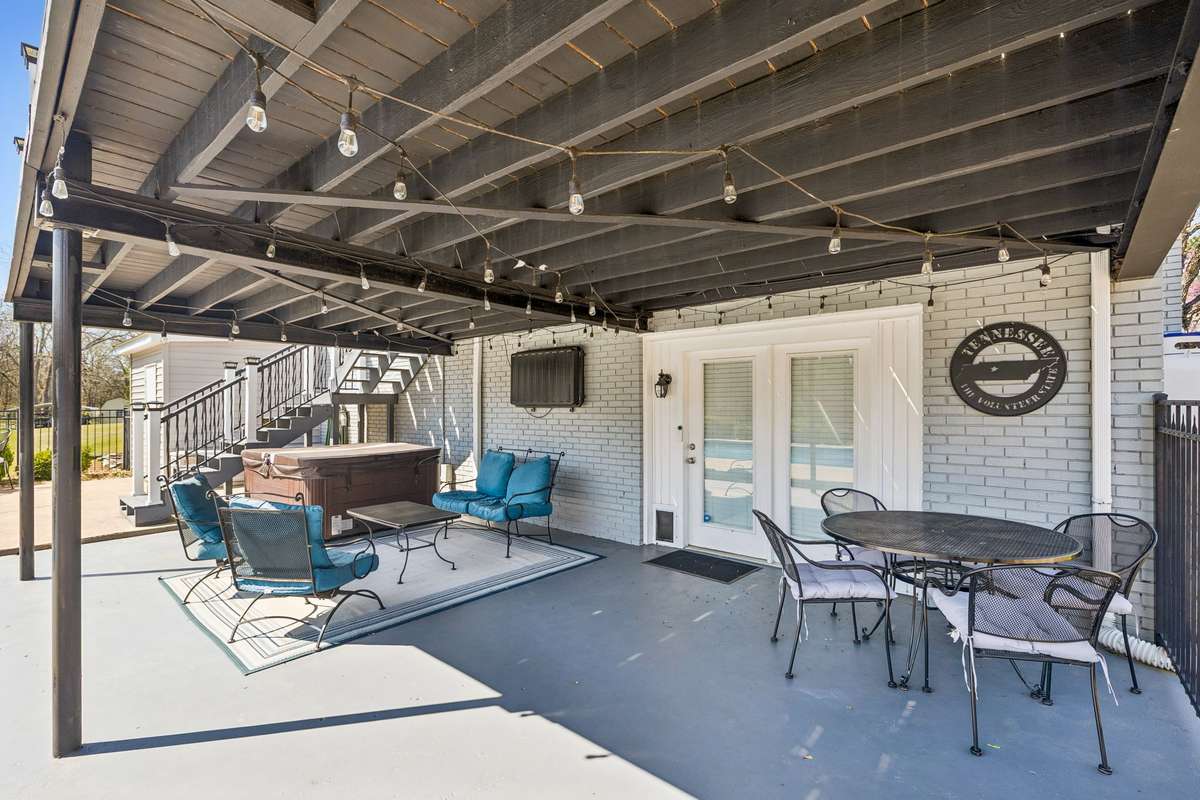 String lights overhead and a metal dining set create an outdoor room that works for morning coffee or evening meals with the wooded backdrop.