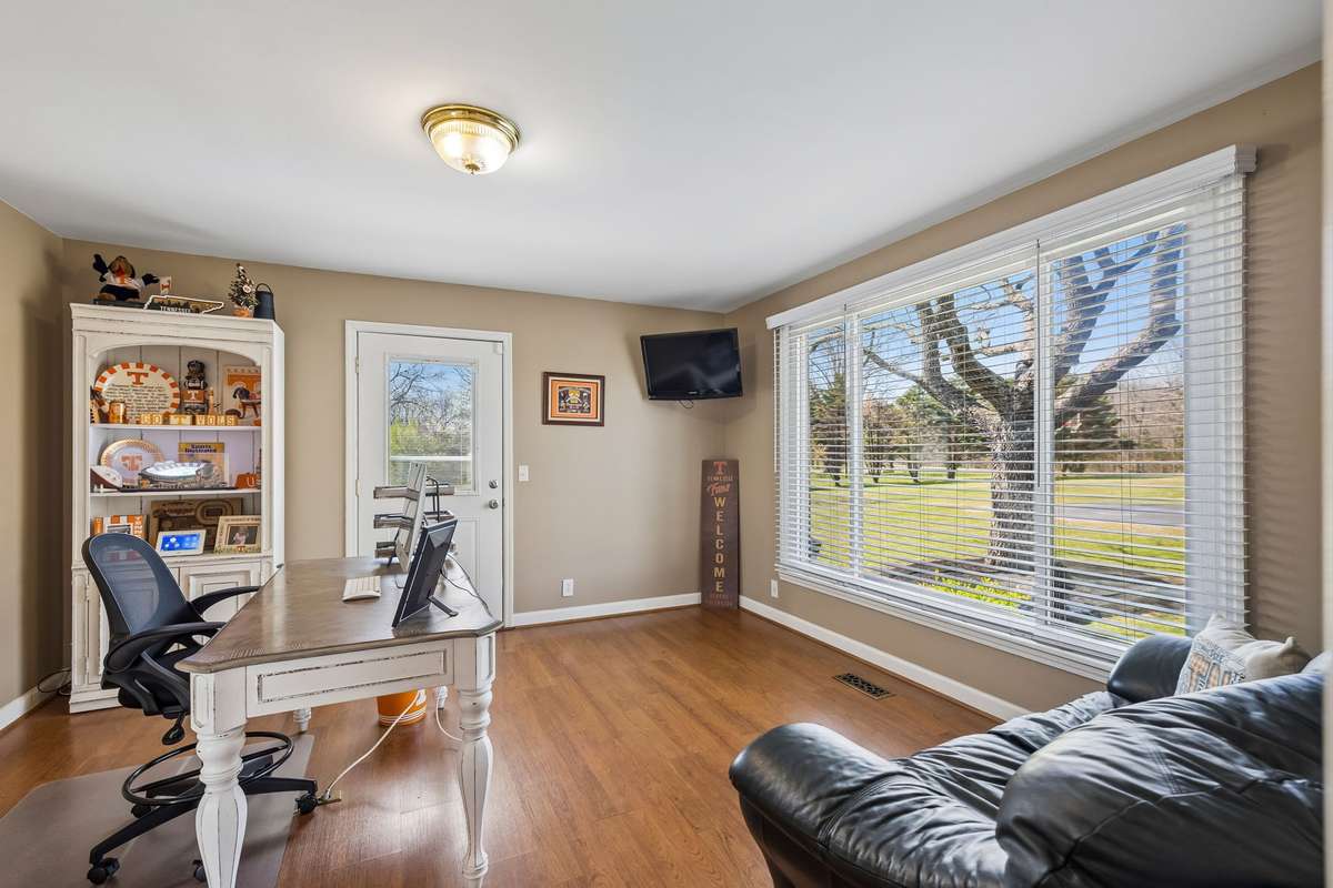 This second office angle shows the comfortable seating area with a leather chair positioned to take advantage of the large windows overlooking the wooded property.