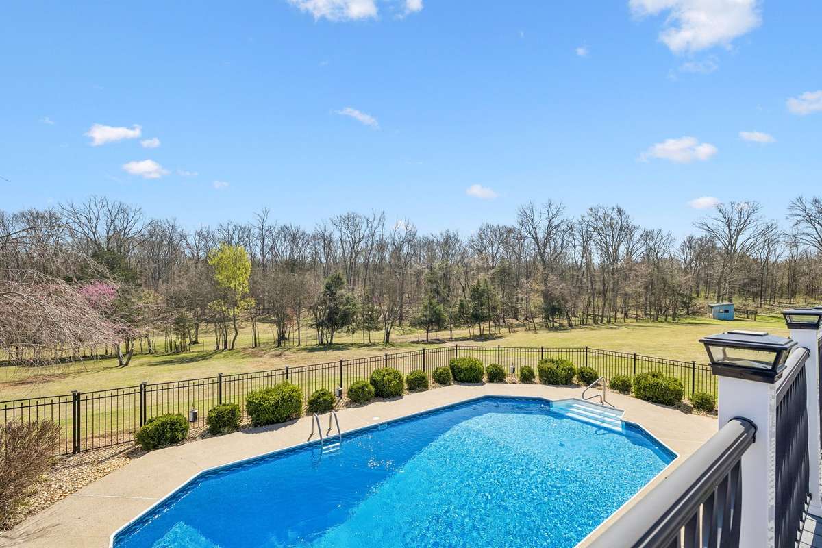 Inground pool surrounded by established landscaping overlooks seventeen acres of wooded property with seasonal color just beginning to emerge.