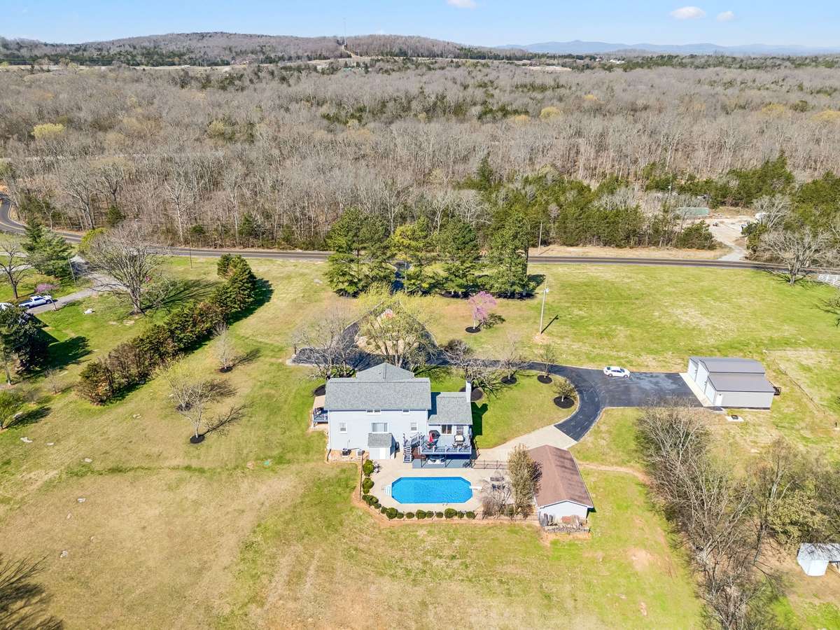 This elevated perspective reveals how the circular driveway and outbuildings create a functional compound layout while preserving the open pasture areas that extend toward the wooded backdrop.