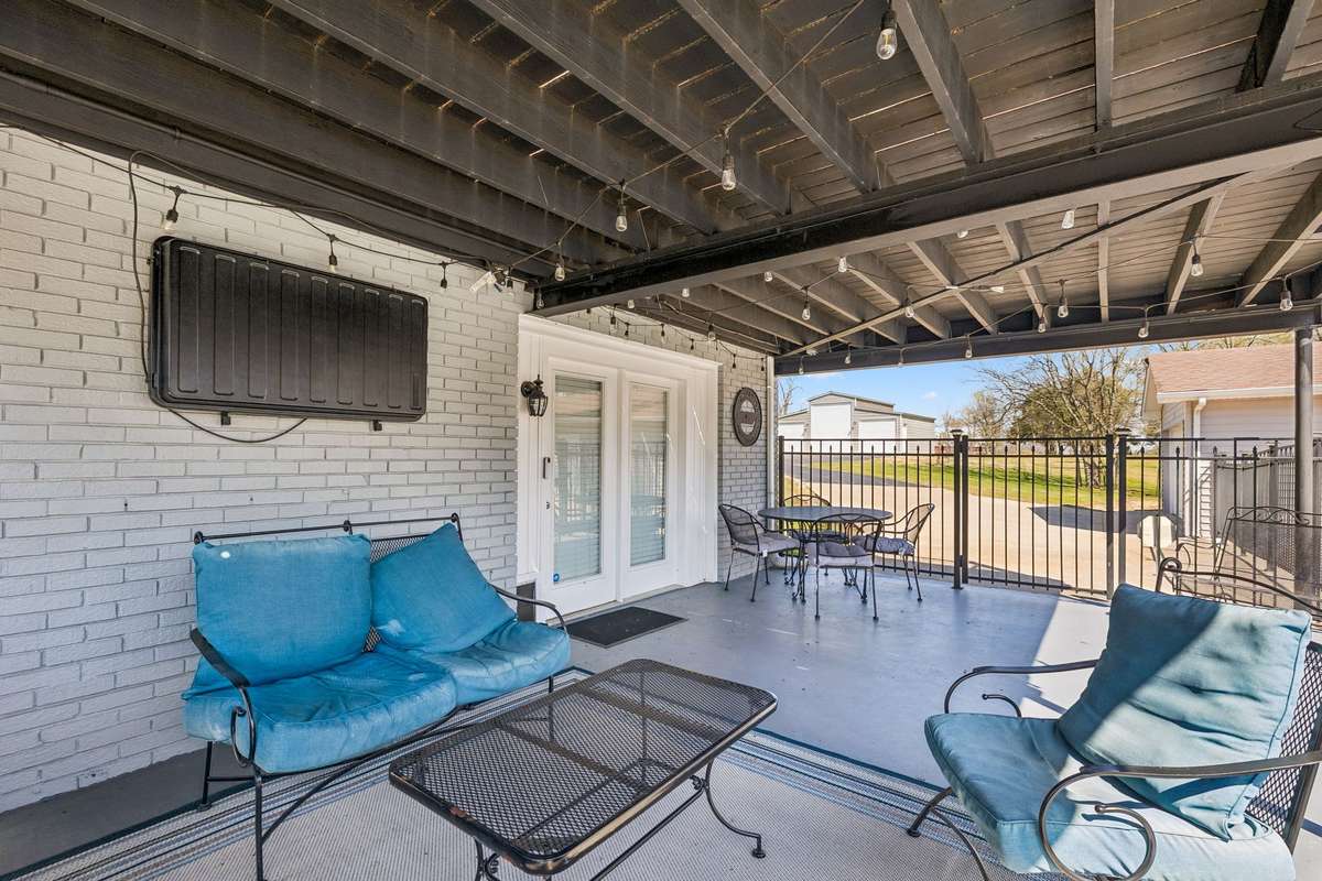 This covered patio extends the living space outdoors with string lighting overhead and views of the 17-acre property beyond the railing.