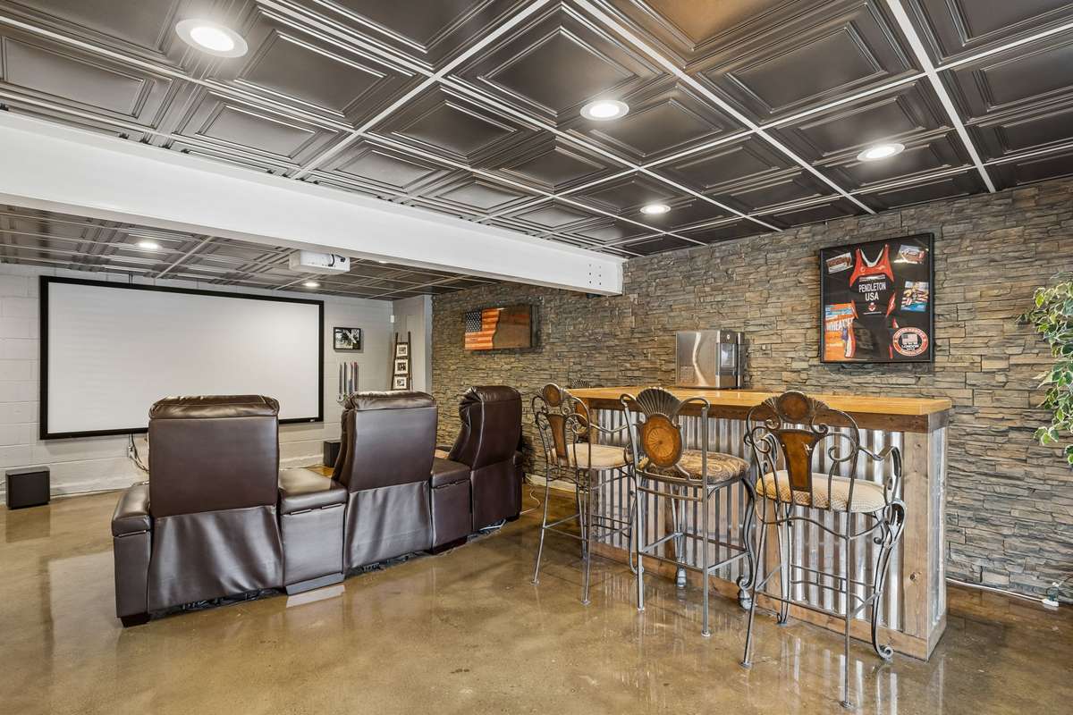 This basement entertainment space combines a theater setup with bar seating and stone accent walls for the complete hangout zone.