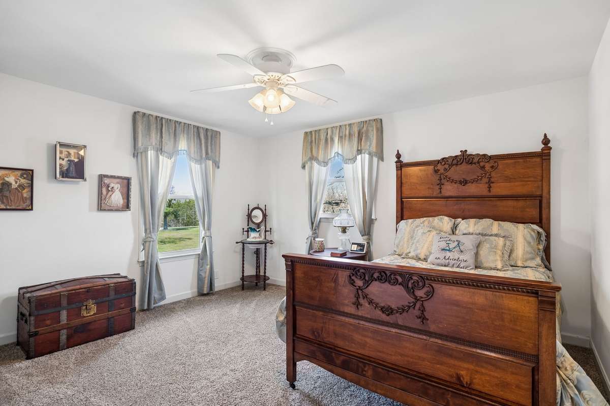 Antique trunk and ornate carved bed frame give this corner bedroom a timeless feel with two windows bringing in natural light from different directions.