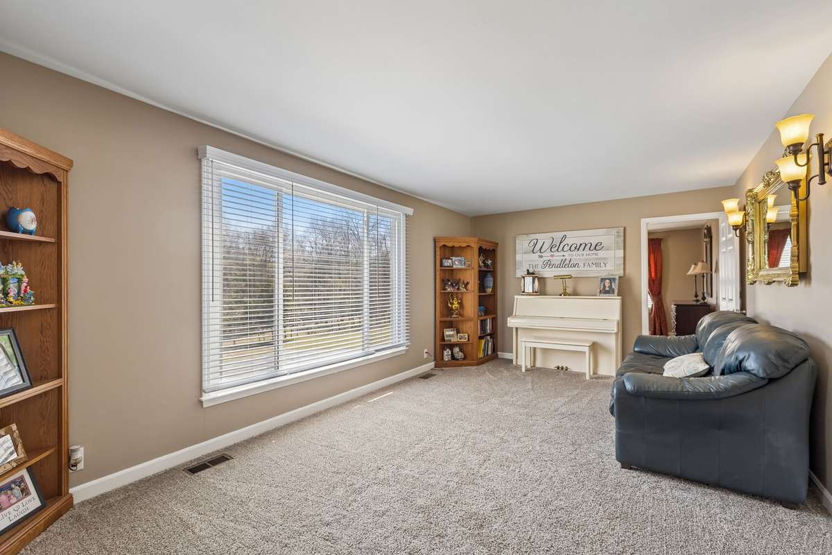 This formal living room with carpet and a large picture window over looking the pool area and the 17 acres.