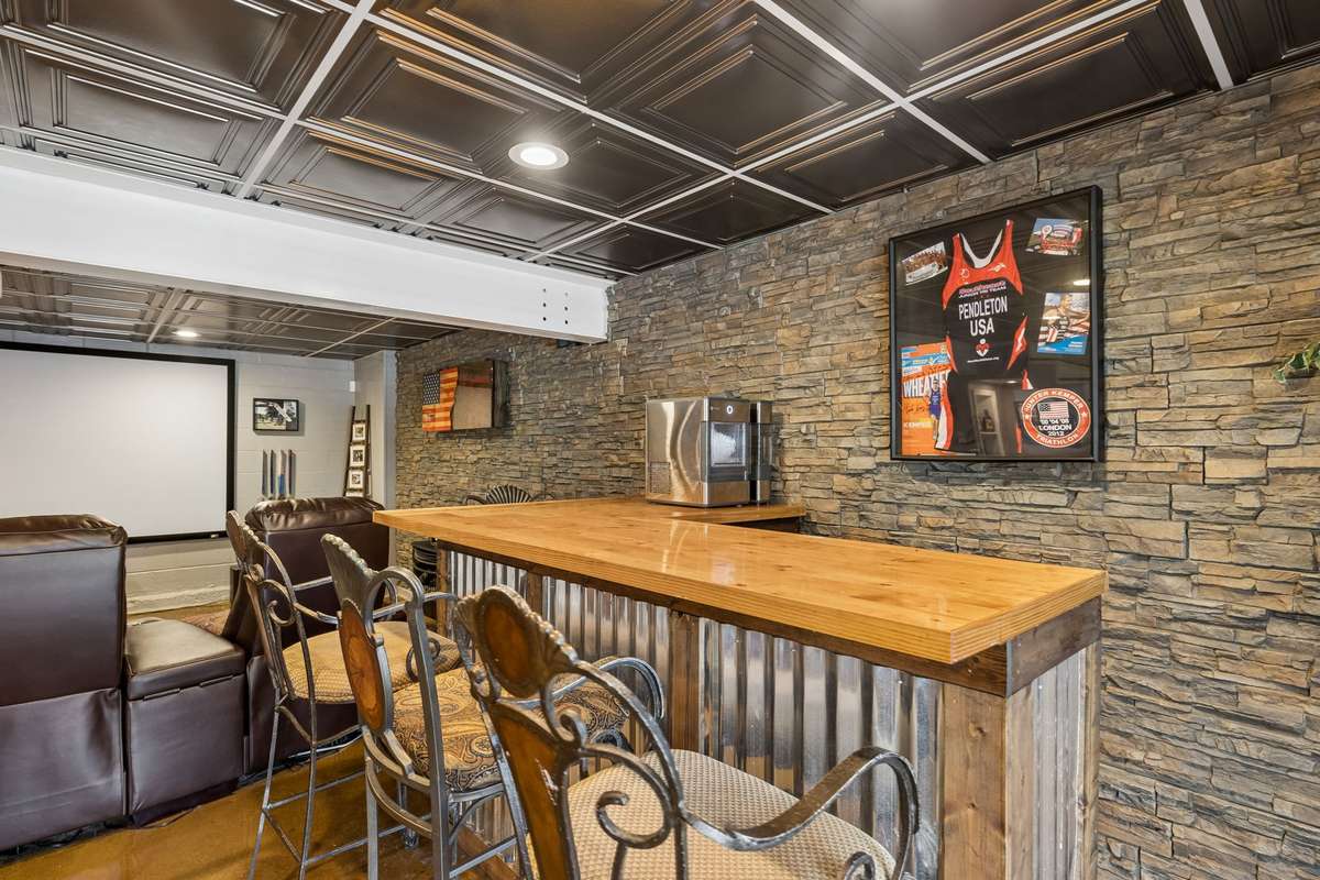 Built-in bar with stone accent wall and decorative ceiling tiles creates a designated entertaining zone in the basement.