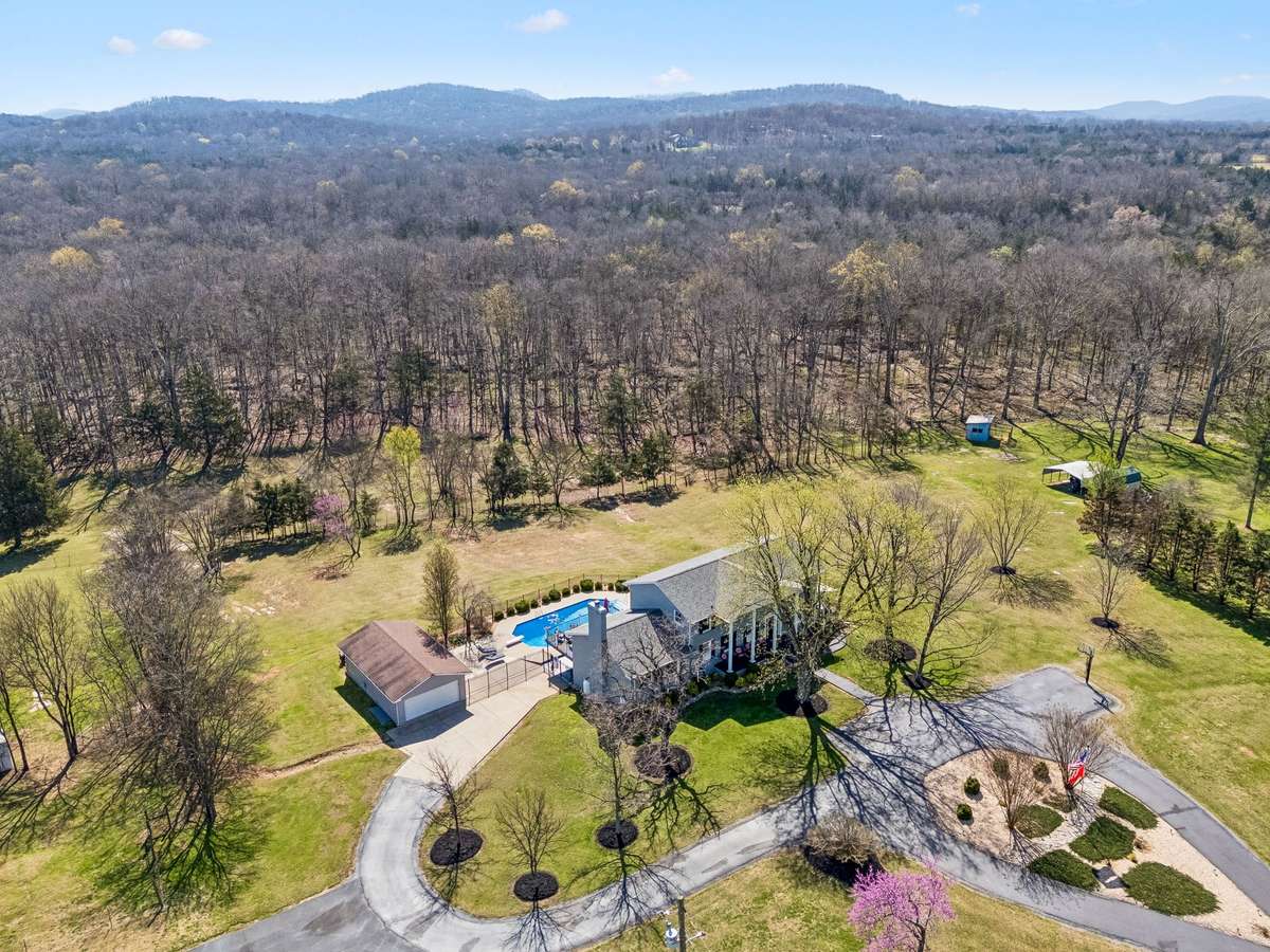 Aerial perspective reveals the home's prime setting on 17 acres with the inground pool and detached workshop positioned to take advantage of the open pasture areas while maintaining privacy from the surrounding wooded hills.
