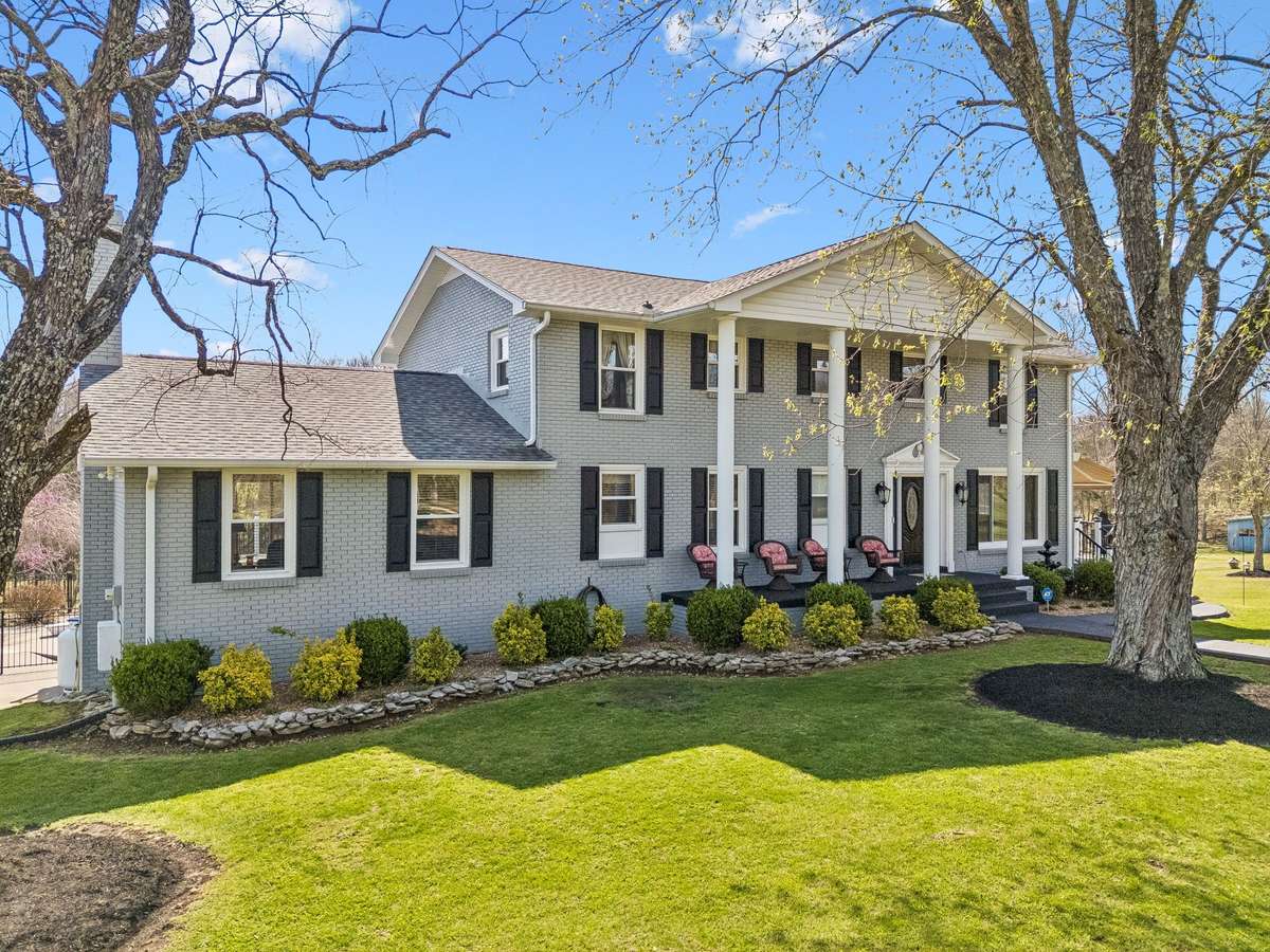 Welcome to 9469 Christiana Fosterville Road, Christiana, TN. Two-story colonial with white columns and a covered front porch on a well-maintained lot with mature trees and landscaped borders.
