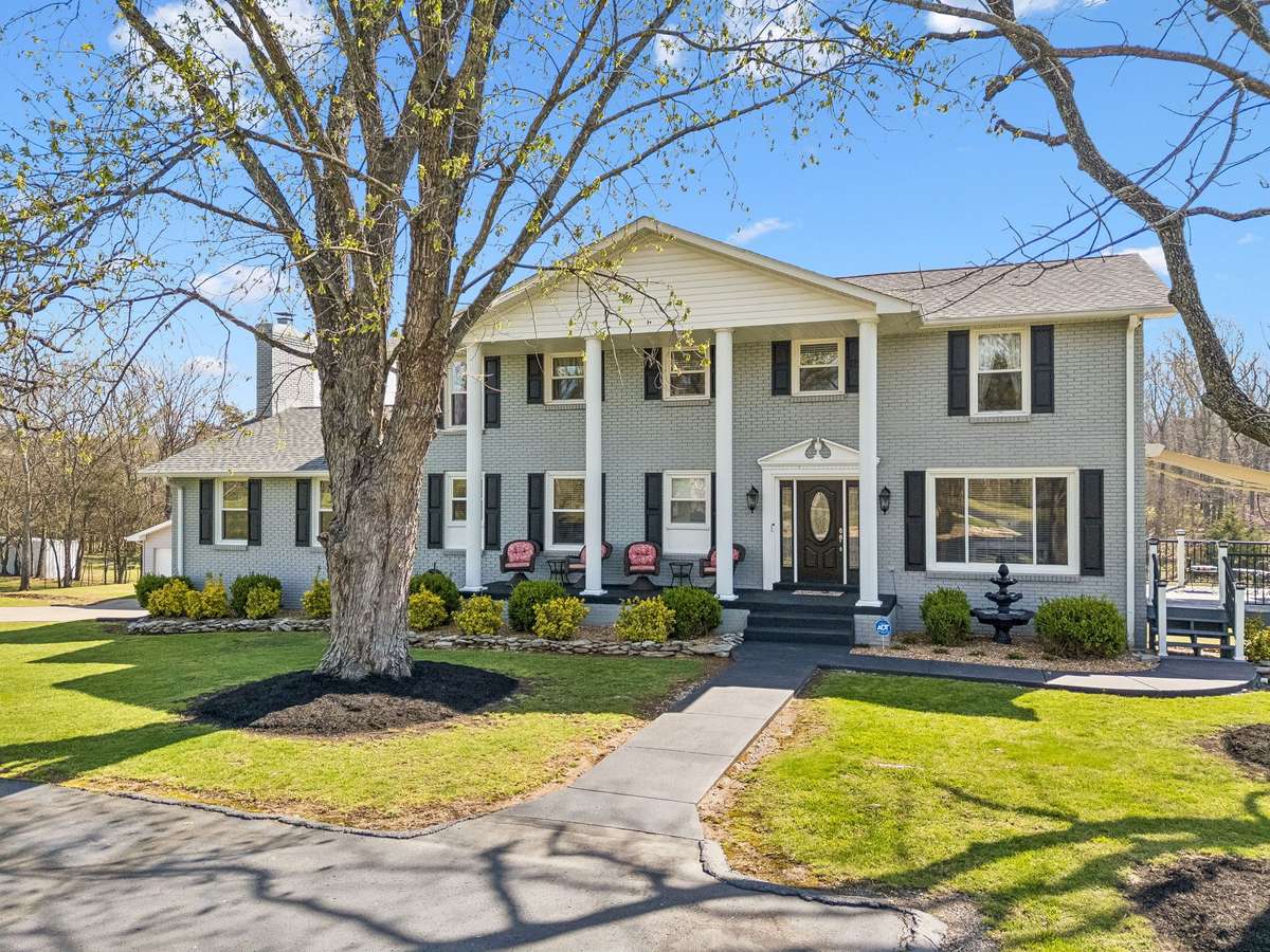 Light gray brick exterior with white columns frames a welcoming front entrance, complete with decorative glass door and classic black shutters.