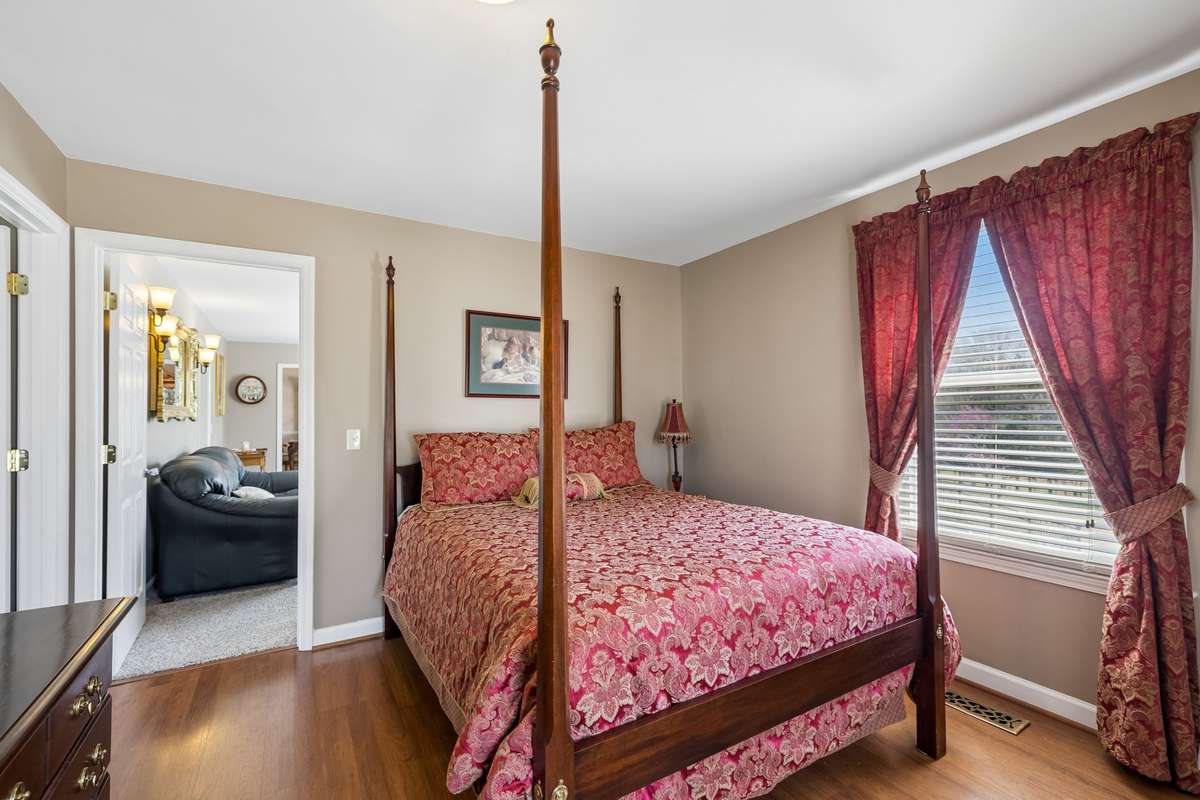 Four-poster bed with matching curtains creates a coordinated look in this upper level bedroom with hardwood floors and natural light from the side window.