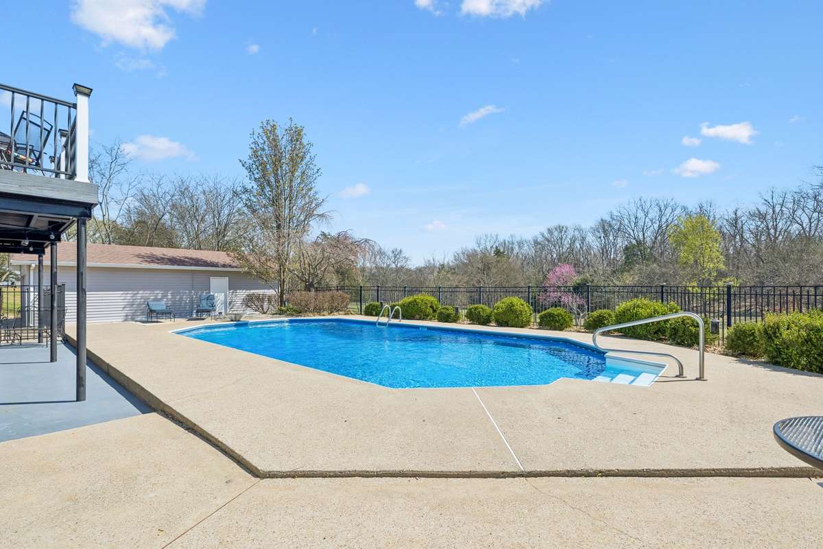 Inground pool with handrails and concrete decking sits behind black fencing with the wooded seventeen acres creating complete privacy for swimming and entertaining.