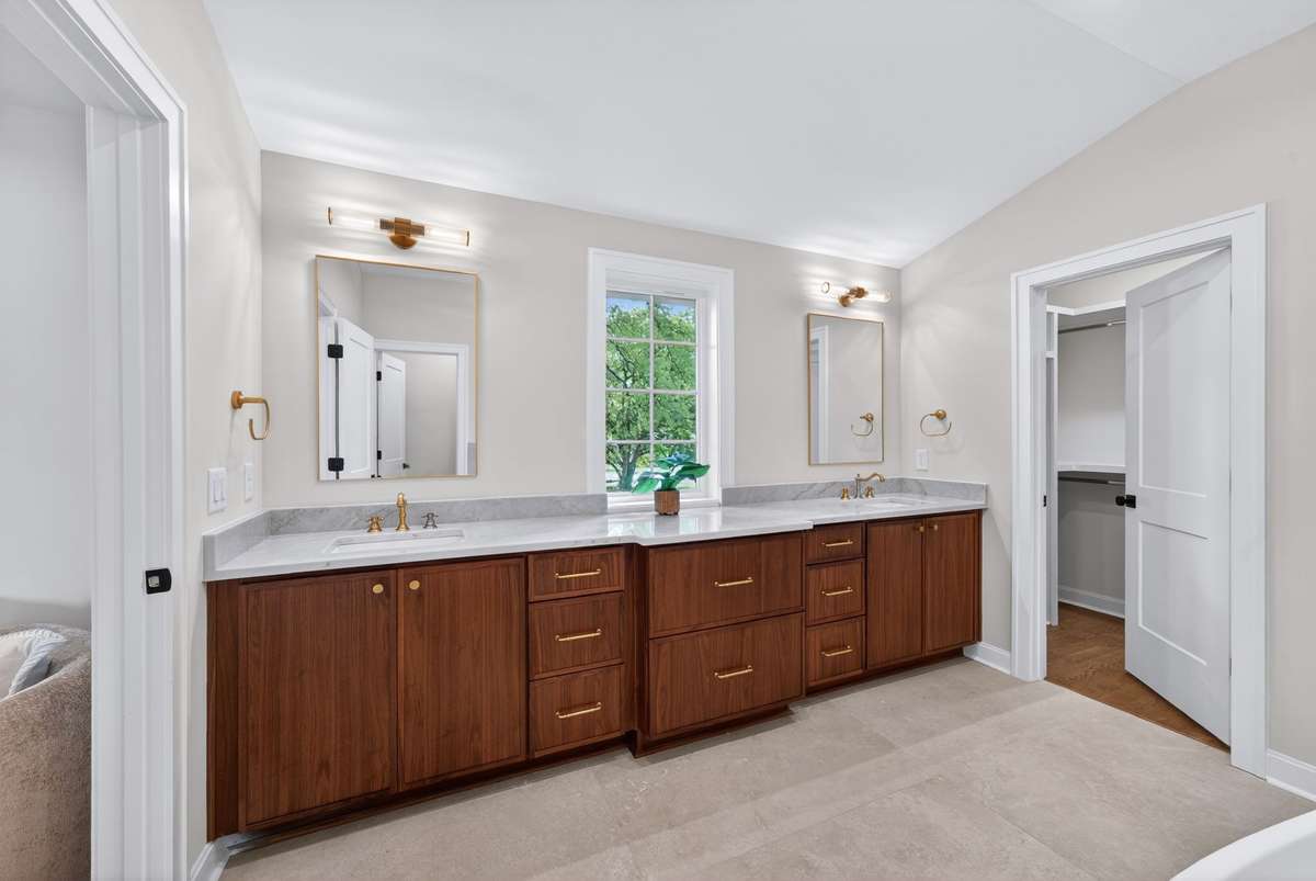 The ensuite bath features dual vanities with walnut cabinetry and abundant storage.