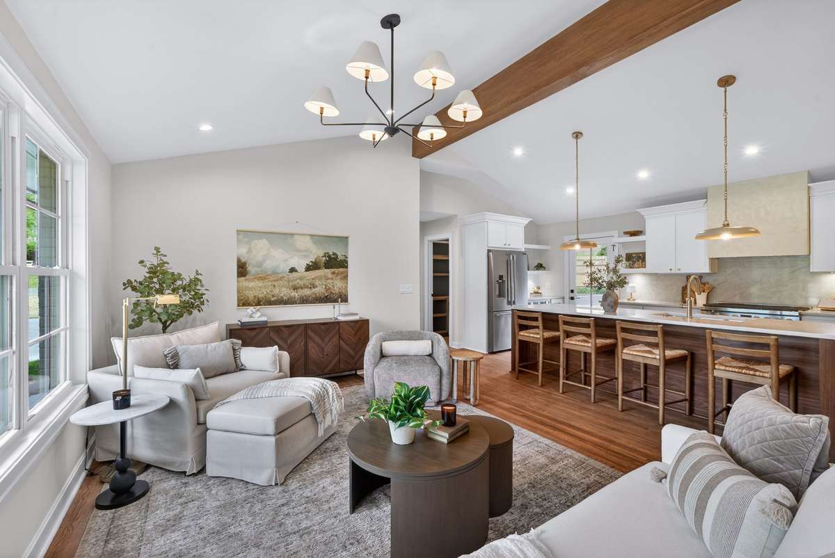 The home features an open layout for the living, kitchen, and dining areas with abundant natural light, vaulted ceilings with a wooden beam, and designer light fixtures.