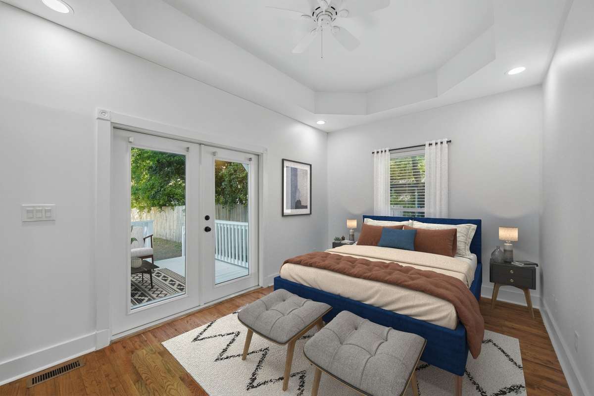 Another view of the bedroom on the main floor, which also has access to the private deck and back yard through the French doors. Notice the tray ceiling and ceiling fan as well. Virtually staged.