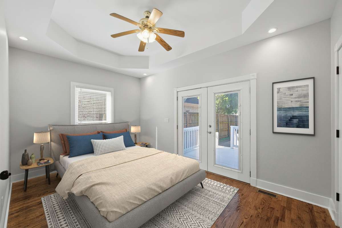 Another view of the bedroom on the main floor, which also has access to the private deck and back yard through the French doors. Notice the tray ceiling and ceiling fan as well. Virtually staged.