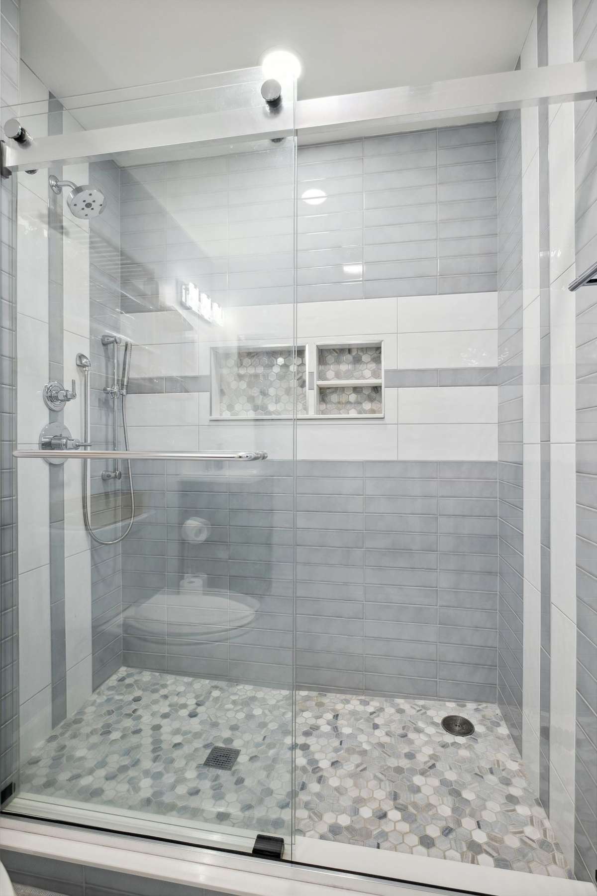 The walk-in shower has two shower heads, shampoo niches and a sliding glass door.
