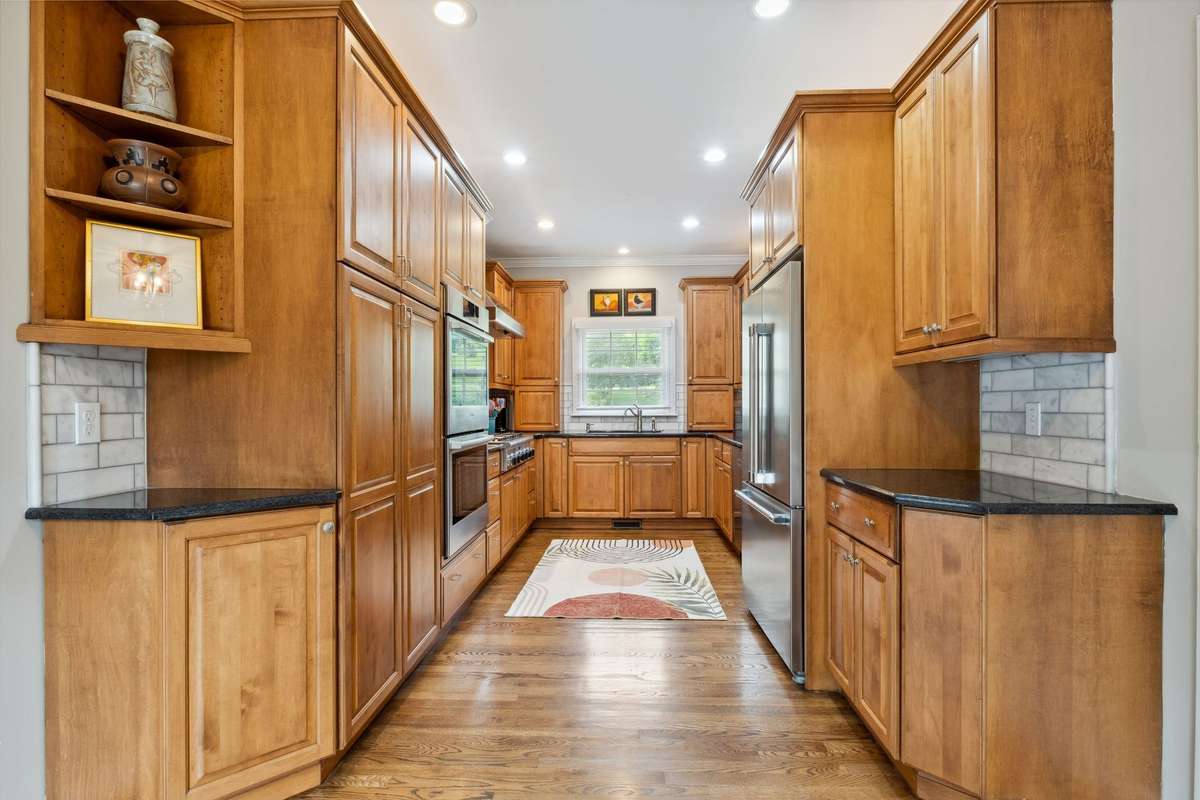 The kitchen is thoughtfully designed to maximize space with custom cabinetry, granite counters and an updated marble backsplash. The cabinetry has pull out pantry shelves, appliance garages, pullout trash bins, open and glass front display cabinets.