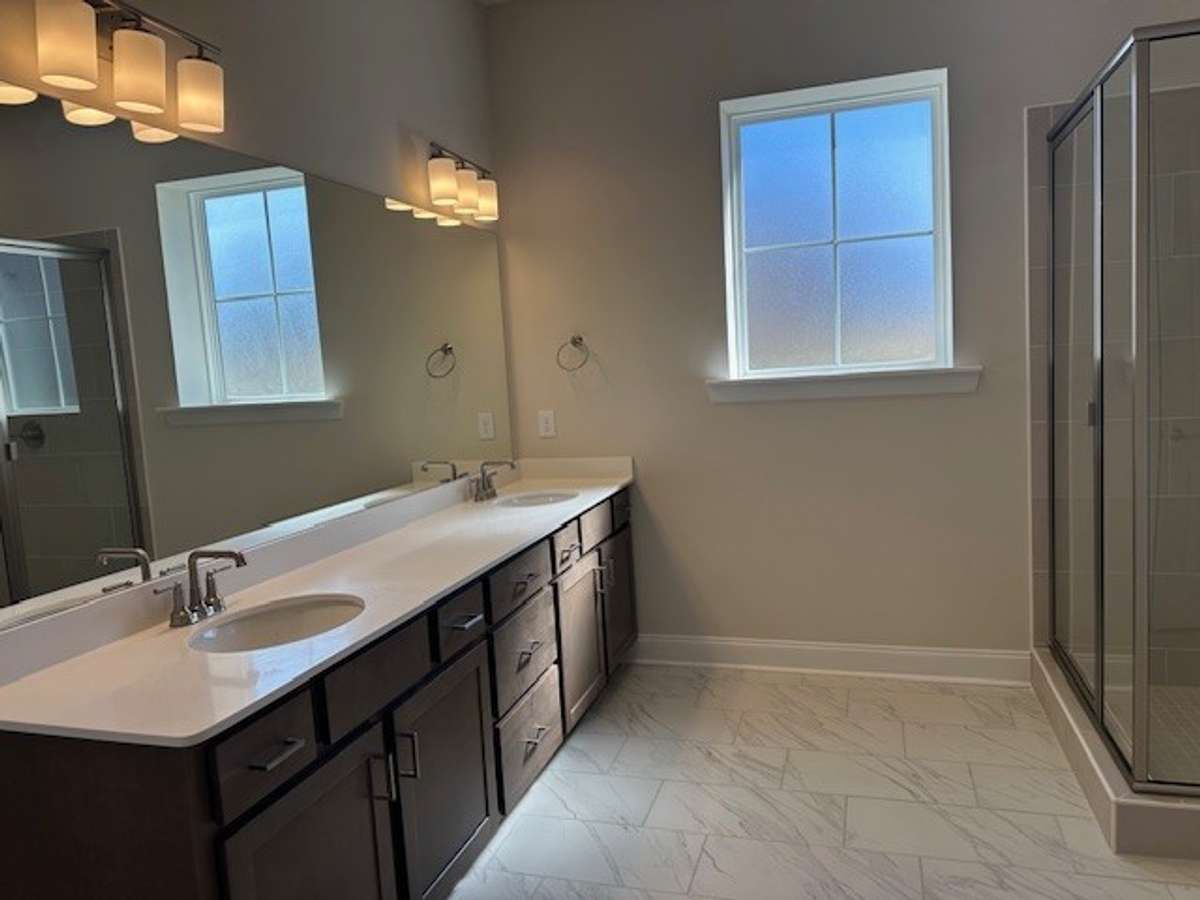 Double sinks with quartz countertops in the Primary Bath, and natural light from the opaque window