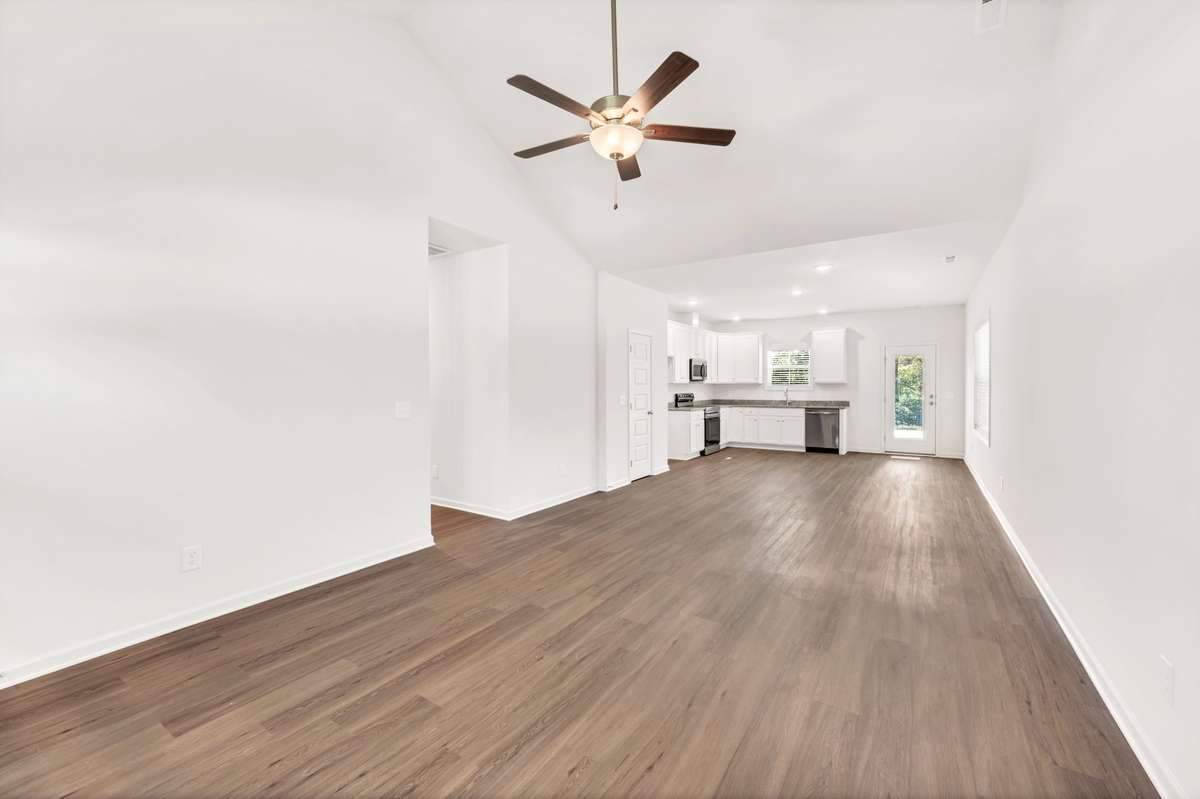 Expansive open floor plan with vaulted ceilings and warm wood-laminate flooring. The bright layout flows into a modern kitchen with white cabinetry and stainless appliances, perfect for entertaining or everyday living. Airy, elegant, and inviting.